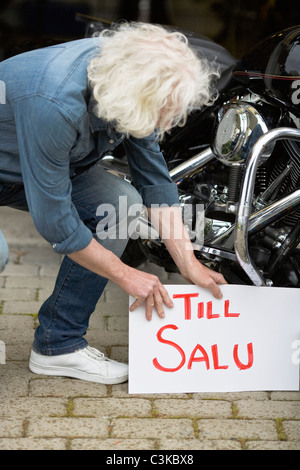 Mann, der für Verkaufsschild mit dem Oldtimer Motorrad Stockfoto