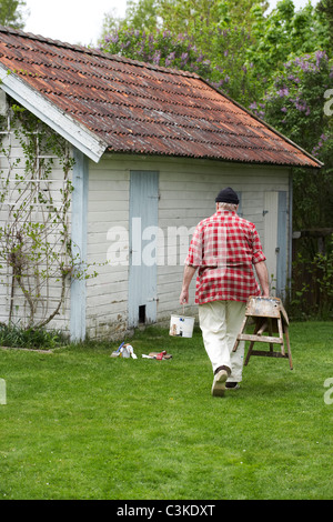 Älterer Mann Malerei seinem Sommerhaus, Schweden. Stockfoto