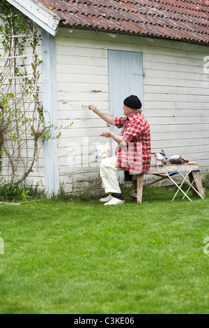 Älterer Mann Malerei seinem Sommerhaus, Schweden. Stockfoto