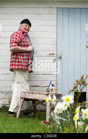 Älterer Mann Malerei seinem Sommerhaus, Schweden. Stockfoto