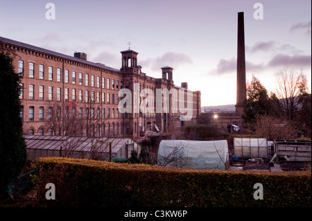 Salts Mill (Schornstein & historische viktorianische Textilfabrik Gebäude & Gewächshäuser in Saltaire Dorf Zuteilungen) bei Sonnenaufgang - Yorkshire, England, Großbritannien. Stockfoto