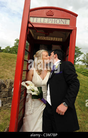 Britische traditionelle Braut und Bräutigam küssen in eine traditionelle rote Telefonzelle am Tag ihrer Hochzeit Stockfoto