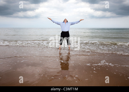 Mann stehend in die Arme des Meeres hob auf der Suche, in den Himmel trug ein Hemd und Hose aufgerollt Stockfoto