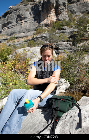 Anglo Frau gilt Sonnencreme für ihren Arm während einer Pause von Wanderung entlang Pecos River in Val Verde County in West-Texas Stockfoto