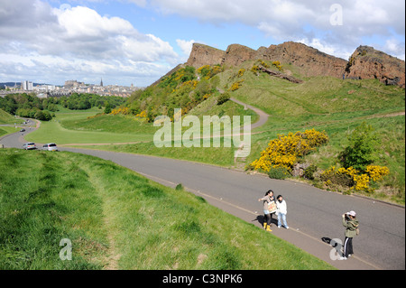 Touristen fotografieren neben Salisbury Crags im Holyrood Park im Zentrum von Edinburgh, Schottland. Stockfoto