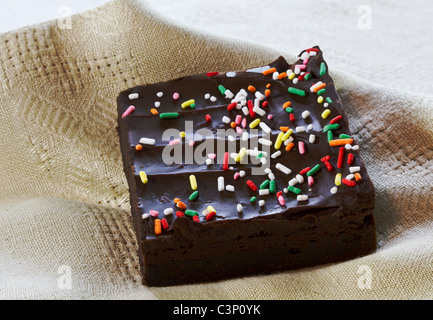 Feuchte, chocolate Brownie schneiden in quadratische Form und mit Streusel auf die dunkle Schokolade Zuckerguss wird auf Beige Leinen Serviette gelegt. Stockfoto