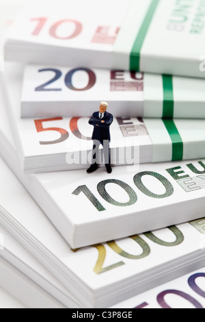 Manager-Figur sitzt auf Stapel von Euro-Banknoten Stockfoto