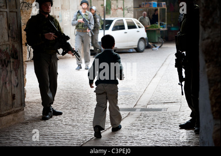 Ein palästinensisches Kind verläuft mitten durch die eine israelische Militärpatrouille in Altstadt von Hebron. Stockfoto