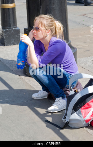 London, Westminster Trafalgar Square, hübsche junge Blondine Tourist in Sonnenbrille ruht Kniebeugen mit Trinkflasche & rucksack Stockfoto