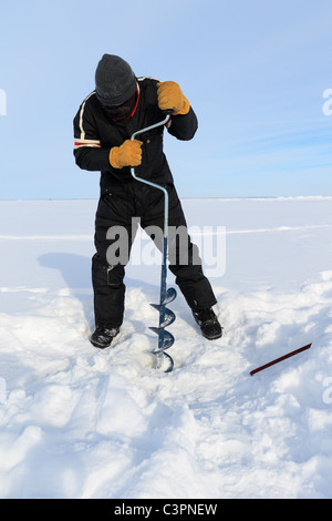 Ein Eis-Fischer mit einem Hand-Schnecke, Bohren Sie eine Loch auf einem zugefrorenen See in Minusgraden Wetter - Minnesota, USA. Stockfoto