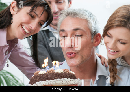 Freunde auf Geburtstagskuchen Kerzen ausblasen Stockfoto