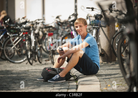 Deutschland, München, Karlsplatz, junger Mann mit Handy, Porträt, Lächeln Stockfoto