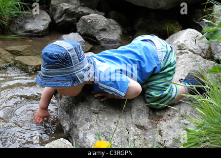 Ein kleiner Junge spielt neben einem Bach. Stockfoto
