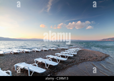 symmetrische aufgereiht weiße Liegestühle auf einer Sandbank am Meer bei Sonnenuntergang Stockfoto