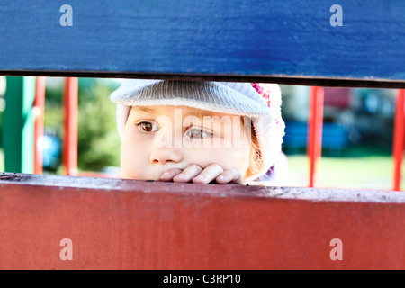 Kleine russische Kind schaut durch einen Spalt zwischen die Holzbohlen Stockfoto