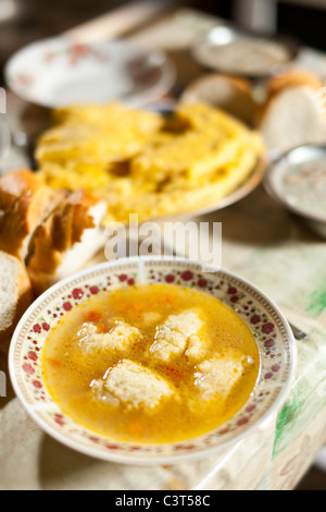 Knödel-Hühnersuppe, traditionelle rumänische Speisen, im Hintergrund ein Teller mit Maismehl Stockfoto