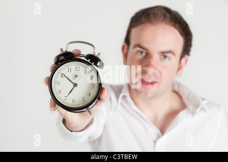 Mann, der Wecker in die Kamera hält. Zifferblatt im Fokus, Mann aus dem Fokus. Stockfoto