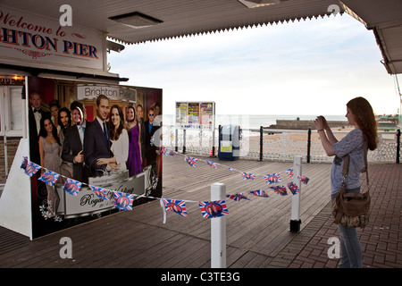 Eine junge Frau fotografiert ihren Freunden durch ein Bild von der königlichen Hochzeit. Brighton Pier, Sussex, England Stockfoto