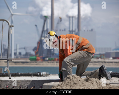 Mann, der auf der Baustelle der Maasvlakte 2, mit große Fabrik im Hintergrund arbeitet. Hafen von Rotterdam, die Niederlande Stockfoto