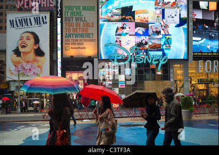 Touristen tragen Sonnenschirme pass Plakate des Broadway-Musicals und der Disney Store an einem regnerischen Tag auf dem Times Square in New York Stockfoto