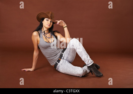 Ein Mädchen in einem Cowboy-Hut sitzt auf braunem Hintergrund Stockfoto