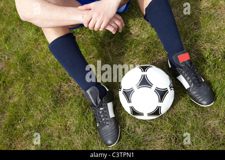 Horizontales Bild des sitzenden Spieler Beine mit Fußball zwischen Stockfoto