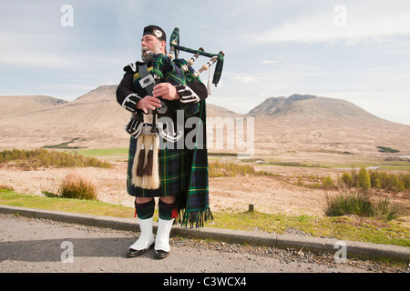 Eine schottische Piper in traditioneller Tracht als Straßenmusikant auf Rannoch Moor in Argyl, Scotland, UK. Stockfoto