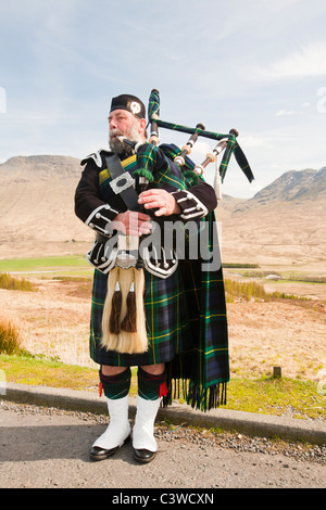 Eine schottische Piper in traditioneller Tracht als Straßenmusikant auf Rannoch Moor in Argyl, Scotland, UK. Stockfoto