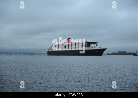 Cunard Kreuzfahrtschiff, Queen Mary 2, dampfend auf dem Hudson River in der Morgendämmerung mit Ellis Island im Hintergrund. Stockfoto