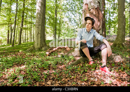 Junger Mann sitzt vor einem Baum im Wald Stockfoto