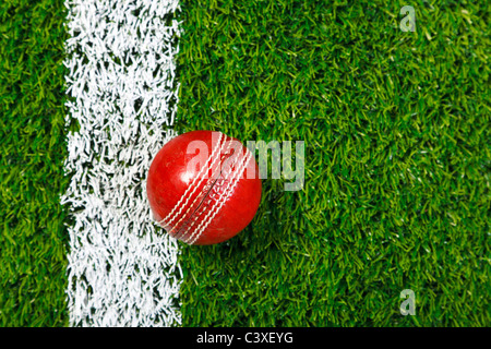 Foto von ein Cricketball auf einer Wiese neben der weißen Linie, von oben geschossen. Stockfoto