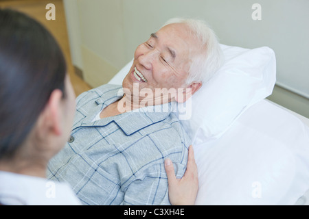 Älterer Mann liegend auf Bett im Gespräch mit der Krankenschwester, die Präfektur Kanagawa, Honshu, Japan Stockfoto