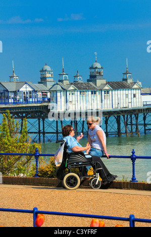 Ältere Frau in einem Rollstuhl im Chat mit einer jüngeren Frau auf Eastbourne Strandpromenade, East Sussex, UK Stockfoto