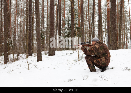 Hunter in Tarnung mit Scharfschützengewehr im Winterwald. Stockfoto