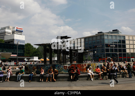 Am Brunnen der 'Freundschaft des Volkes', der von Walter Womacka (1970 ) entworfen wurde, sitzen Menschen auf dem Alexanderplatz im zentralen Berliner Bezirk Mitte Stockfoto