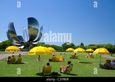 Die Menschen sitzen unter gelben Schirmen in der Nähe der Floralis Generica Skulptur am Plaza de Las Naciones Unidas, Buenos Aires, Argentinien. Stockfoto