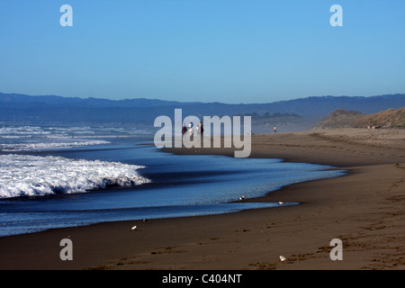 Menschen, die Reitpferde auf Moss Landing State Beach in der Nähe von den pazifischen Ozeanwellen Stockfoto