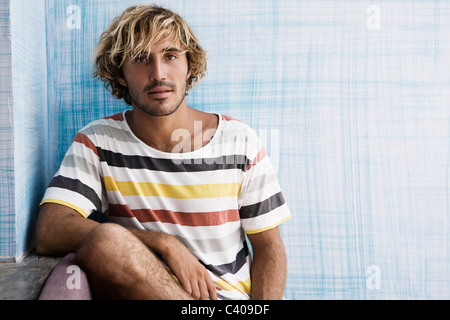 Kerl sitzt an blauen Wand, auf der Suche in der Kamera Stockfoto