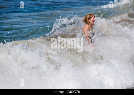 Eine lachende Frau springt durch eine brechende Welle in Riviera Nayarit Lo de Marcos Pazifik Küste. Stockfoto