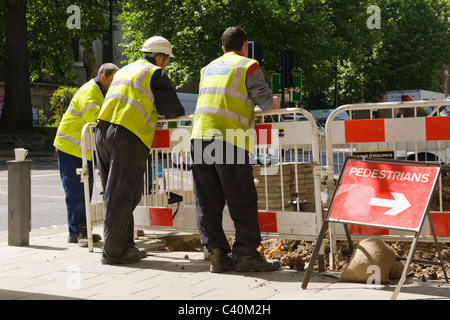 London Kings Cross, britische Arbeiter in Sicherheit Jacken Uhr Graben Mannloch auf Euston Road Bürgersteig mit Tee Tassen auf post Stockfoto