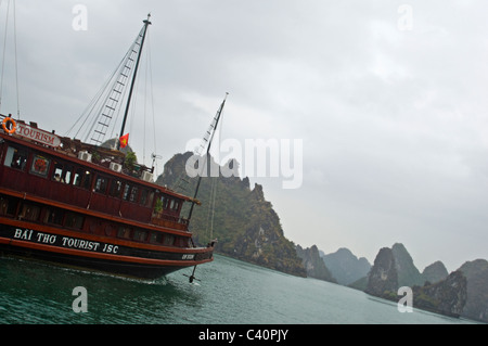 Horizontale Ansicht von Kalkstein Karst (Felsen) in Halong-Bucht und einer traditionellen hölzernen Dschunke verwendet für Reiseleiter Segeln übergeben. Stockfoto