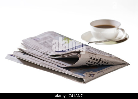 Gefaltete Zeitung auf weißem Hintergrund, mit einer Tasse Kaffee. Stockfoto