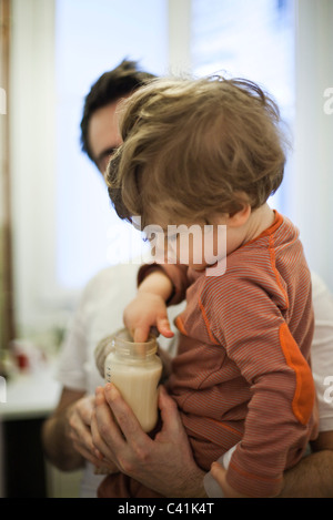 Kleinkind Jungen in den Armen des Vaters, testen Milchtemperatur in Baby-Flasche Stockfoto