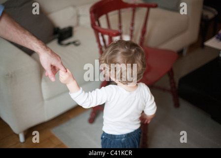 Kleinkind festhalten an Vater seiner Hand, zu Fuß in Richtung Sofa, beschnitten Stockfoto
