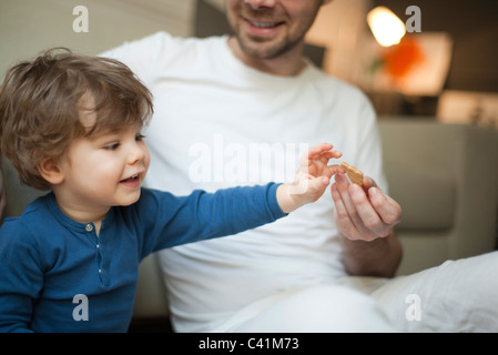 Kleinkind Jungen für Cookie in der Hand des Vaters zu erreichen Stockfoto