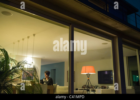 Mann mit Laptop im Wohnzimmer, durch Fenster angezeigt Stockfoto