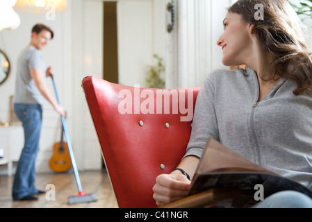 Frau im Mann über Schulter lächelnd, als er den Boden fegt Stockfoto