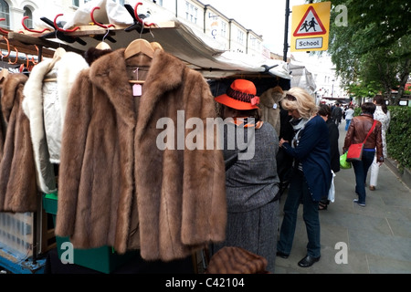 Eine Frau einkaufen und Markt Händler auf einem Vintage-Fell Mantel Jacke zum Verkauf auf einer Portobello Road antike Kleidung Marktstand für alte Pelzmäntel in Notting Hill West London ENGLAND GB KATHY DEWITT Stockfoto