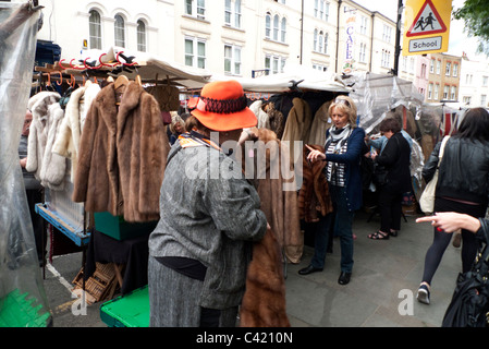 Menschen kaufen Jahrgang Pelzmäntel und Jacken auf ein Portobello Road Market stall Notting Hill London England UK Stockfoto