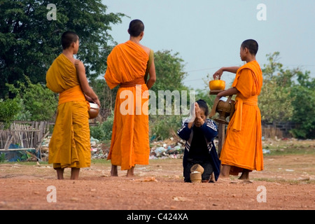 Eine Gruppe buddhistischer Mönche stehen auf einer unbefestigten Straße während des Empfangs Reis von einer Frau in kommunistische Laos. Stockfoto